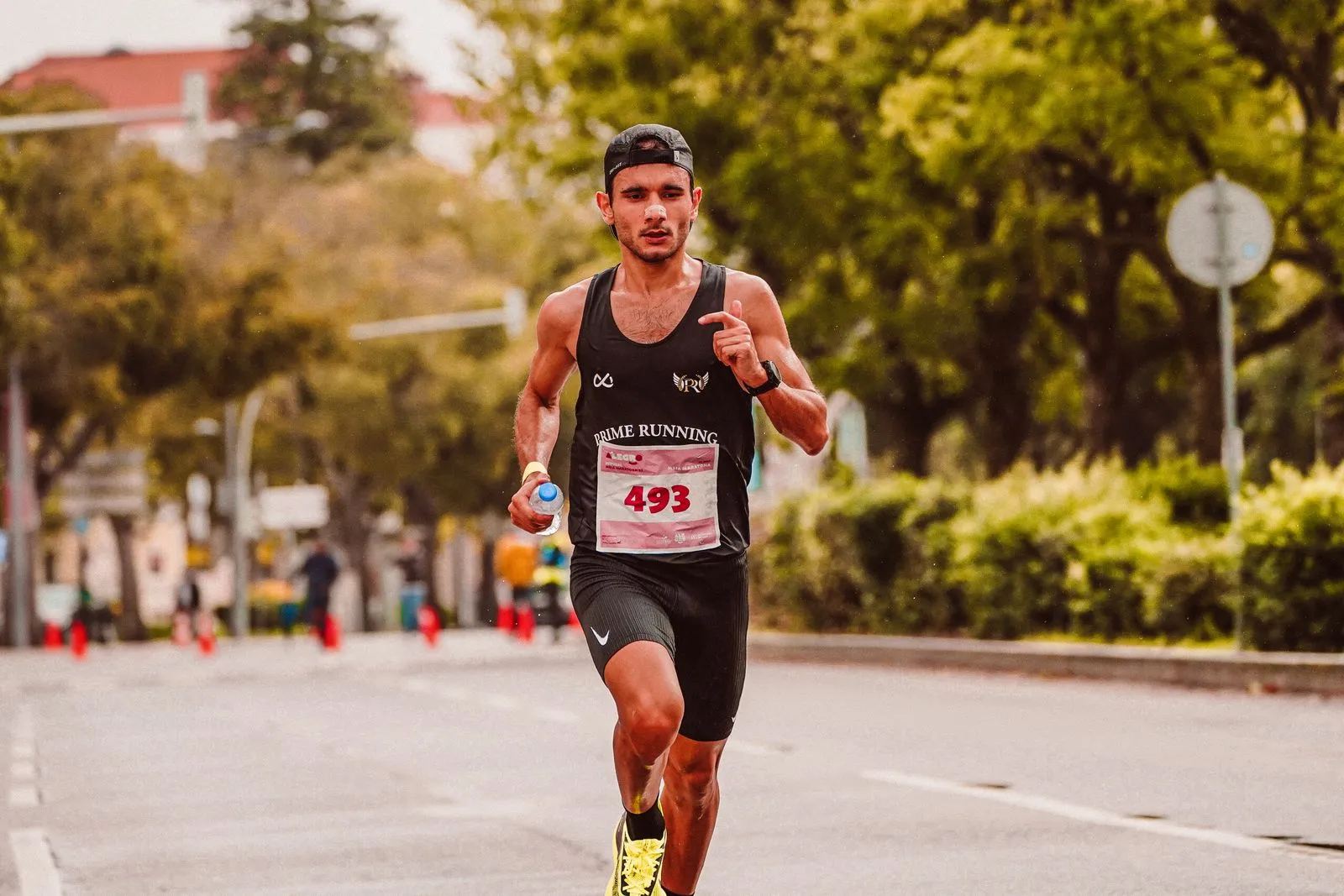 Focused male athlete running in a marathon, wearing a tank top and holding a bottle of water.